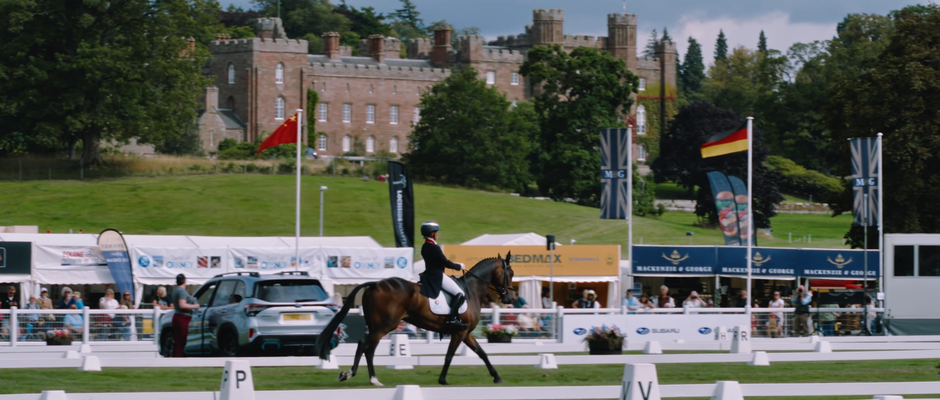 A dressage rider on a bay horse at the Scone Palace International Horse Trials, the castle on the hill behind them.